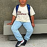 child, boy, smiling, sitting, bench, backpack, school, t_shirt, jeans, sneakers, gap_tooth, portrait, outdoor, wall, concrete, floor, casual_clothing, schoolchild, happy, single_person