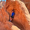 child, boy, outdoor, sandstone, rock_formation, canyon, desert, hiking, adventure, travel, nature, landscape, blue_sky, sunlight, orange_rock, seated, sportswear, hat, sneakers, portrait