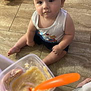 Zaidyn joined the competition — help win amazing prizes! baby, child, food, baby_food, spoon, floor, tile, toy, cushion, hand, container, clothing, sitting, indoor, feeding, curious, face, mouth, eyes, person