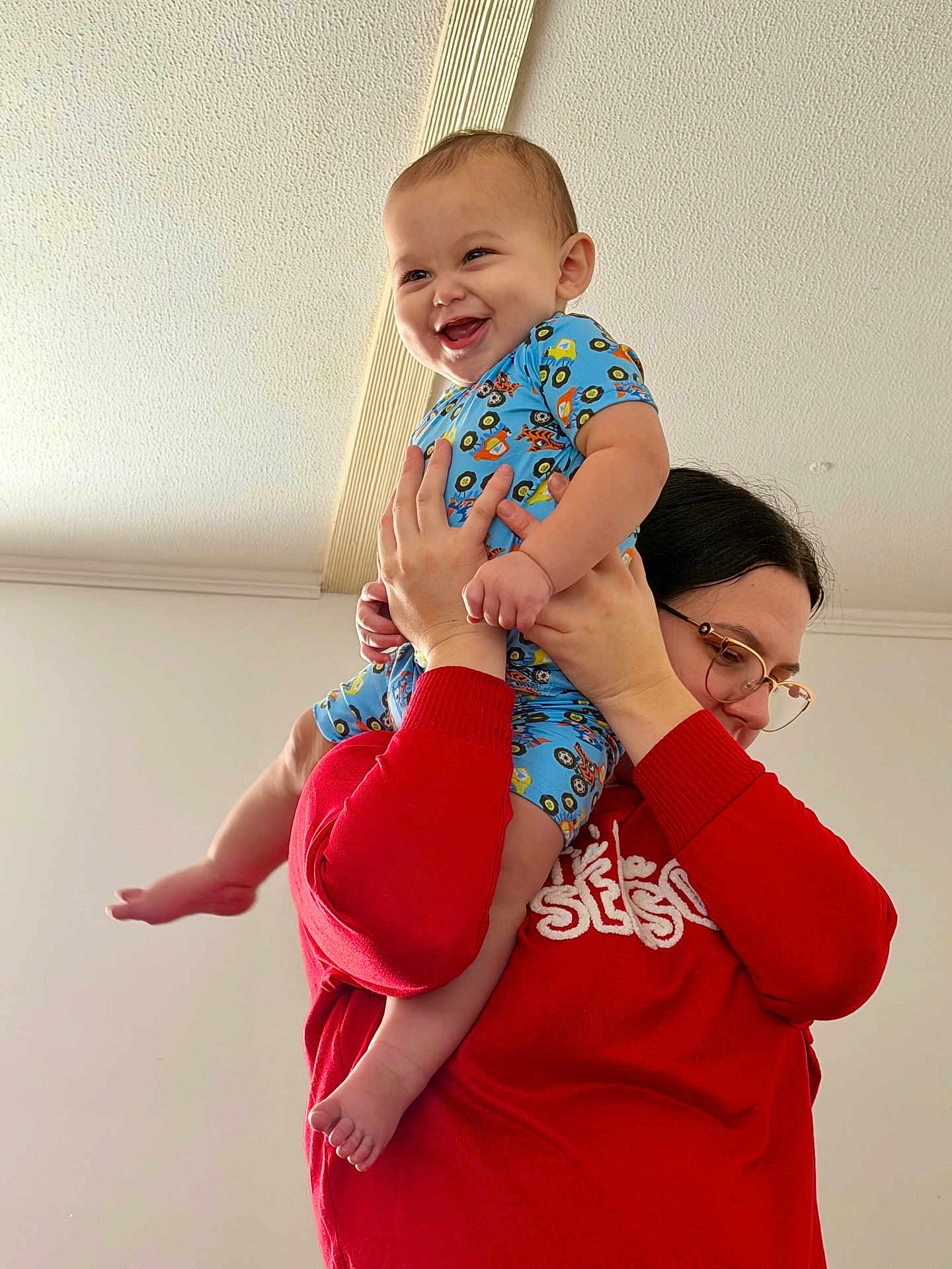 Sawyer is registered to the contest to win money with this photo: baby, child, person, indoor, smile, happy, lifting, blue_clothing, red_sweater, glasses, hand, foot, ceiling, playful, joyful, cute, holding, infant, family, casual