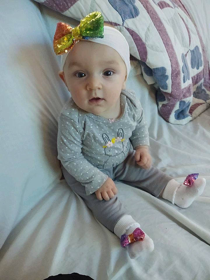 Gabi is registered to the contest to win money with this photo: baby, baby_toddler_clothing, cap, comfort, dress, eye, face, grass, happy, head, headband, headpiece, headwear, human_body, jewellery, linens, person, pink, plant, sitting