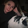 woman, cat, indoor, selfie, black_and_white_cat, curious, face, portrait, closeup, dim_lighting, tattoo, casual, resting, relaxed, animal, pet, home, night, expression, feline