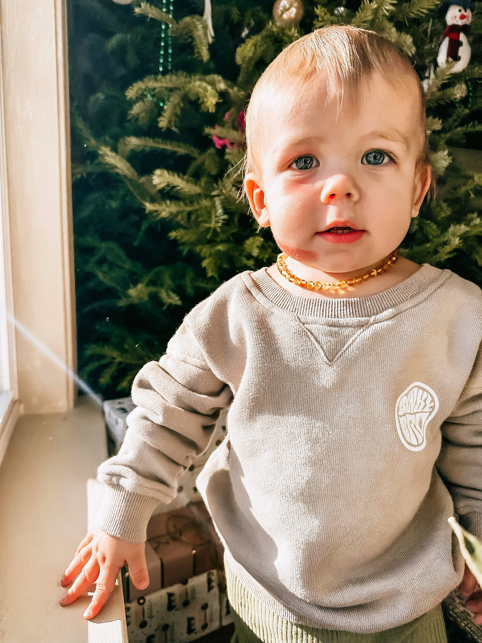 Lennon is registered to the contest to win money with this photo: baby, baby_toddler_clothing, cheek, child, grass, happy, head, human_body, lip, neck, ornament, outerwear, pattern, person, sitting, skin, sleeve, t_shirt, toddler, white