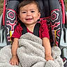 Skylar is registered to the contest to win money with this photo: baby, child, smiling, blanket, car_seat, outdoor, grass, stroller, happy, person, infant, red_clothing, patterned_fabric, seatbelt, portrait, cute, young_child, warm, cozy, comfort