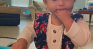 Skylar joined the competition — help win amazing prizes! toddler, child, indoor, floor, blue_object, hand_in_mouth, ponytail, floral_dress, long_sleeve_shirt, living_room, window_blinds, couch, table, tiles, cute, kneeling, home, baby, person, young_child