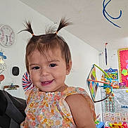 Skylar is registered to the contest to win money with this photo: child, toddler, smile, pigtails, flower_dress, indoor, playroom, toys, colorful, learning_materials, clock, wall_decor, person, cute, baby, happy, portrait, playful, furniture, education