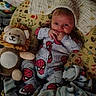 baby, infant, spiderman_onesie, plush_toy, lion_toy, blanket, pillow, patterned_fabric, child, cute, indoor, portrait, baby_clothing, soft_toy, lying_down, hand_to_mouth, curious, face, baby_bedding, cozy