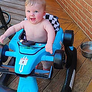 Mateo joined the competition — help win amazing prizes! baby, child, blue_toy_car, toy, outdoor, wooden_deck, brick_wall, happy, smiling, person, infant, playtime, seat, wheels, metal_bowl, hair, face, hands, baby_joy, candid