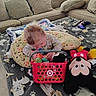 Mateo is registered to the contest to win money with this photo: toddler, child, toy_basket, colorful_toys, mickey_mouse, plush_toy, blanket, dog_pattern, couch, cushions, remote_control, gaming_controller, indoor, living_room, curly_hair, floor_play, soft_toys, pillow, child_playing, casual_clothing