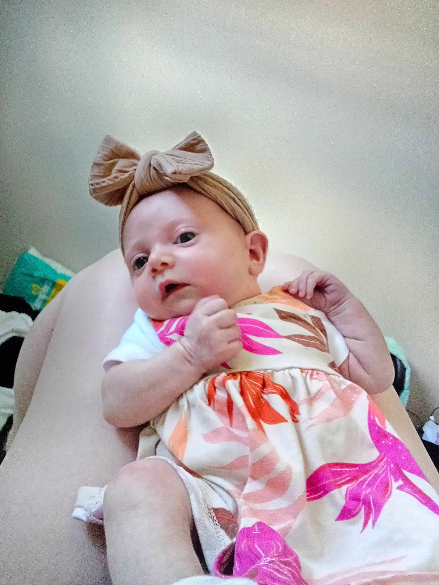 Aurora is registered to the contest to win money with this photo: baby, infant, bow_headband, floral_dress, legs, skin, hand, face, person, clothing, indoor, cute, newborn, child, pink, orange, white, pattern, portrait, resting