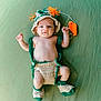 Charlie is registered to the contest to win money with this photo: baby, infant, newborn, crochet_hat, knit_booties, handmade_clothing, green_background, lying_down, portrait, cute, bare_torso, toy, orange_toy, hat, smile, looking_up, cozy, studio_style, small_hands, adorable