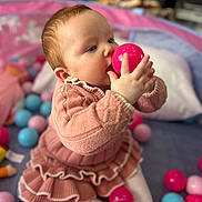 Elsie-Mae joined the competition — help win amazing prizes! baby, child, pink_sweater, knitted_clothing, ball_pit, colorful_balls, pink_ball, blue_ball, play_area, indoors, soft_focus, cute, toddler, seated, hand, face, curious, playtime, warm_lighting, cozy