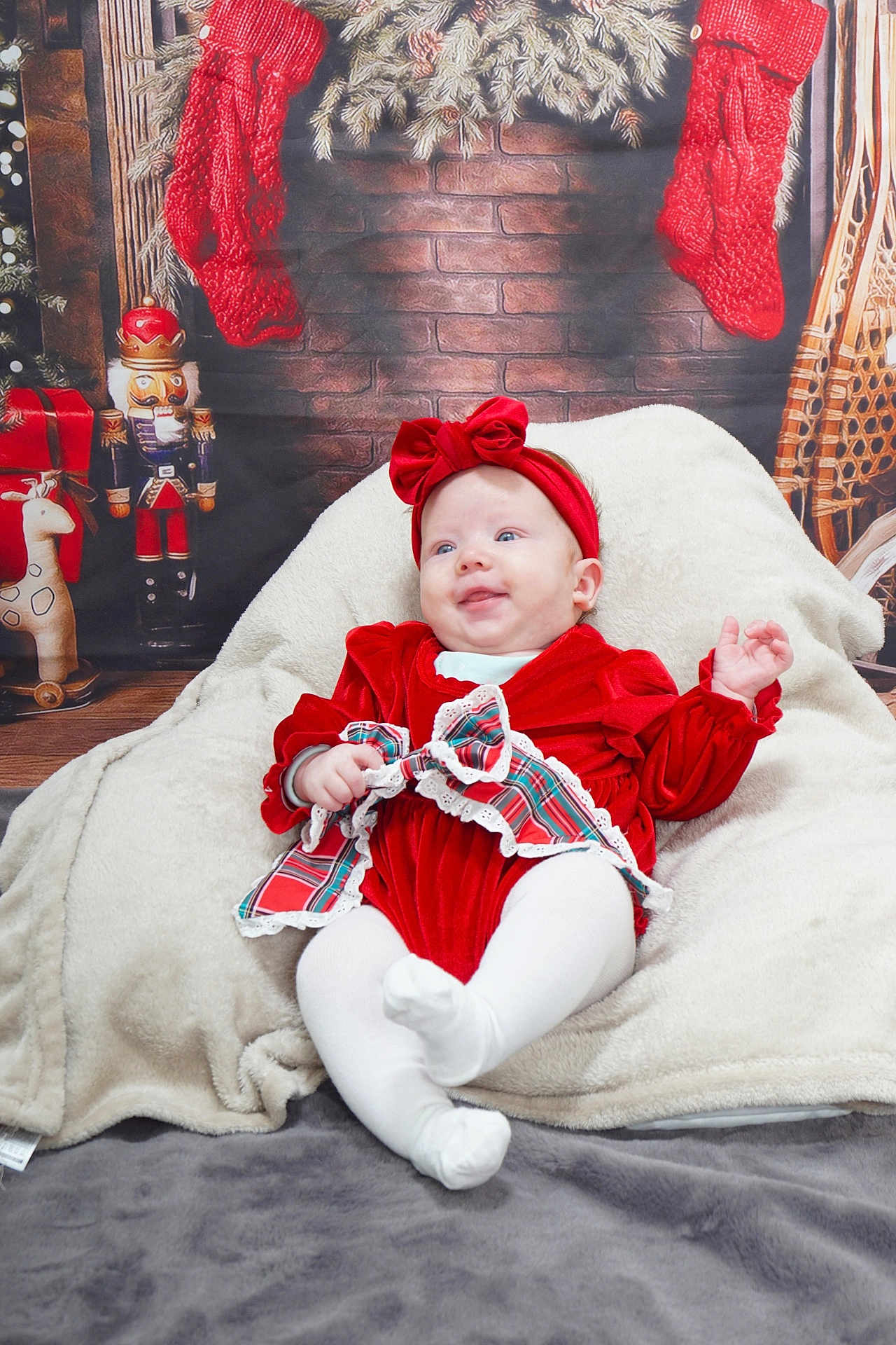 Elsie-Mae joined the competition — help win amazing prizes! baby, red_clothing, headband, blanket, christmas_stockings, nutcracker, holiday_decor, plaid_bow, white_tights, smiling, infant, festive, cozy, indoor, brick_wall_background, wooden_floor, toy_giraffe, snowshoes, portrait, cute