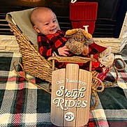 Jaxzen joined the competition — help win amazing prizes! baby, plush_toy, basket, fireplace, christmas_stocking, plaid_pajamas, blanket, wooden_sign, holiday_decor, indoor, smiling, child, cute, festive, toy, cozy, warm, sleigh, red, black