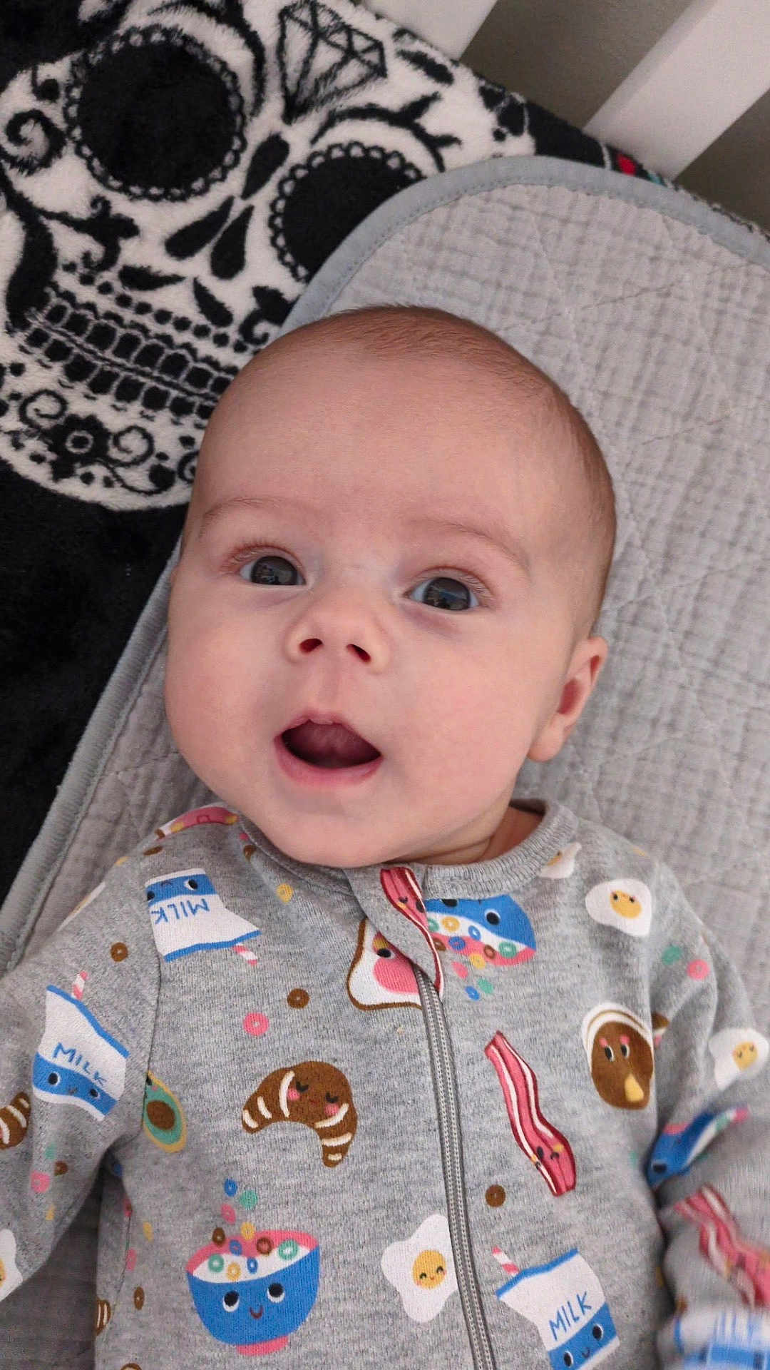 Jaxzen joined the competition — help win amazing prizes! baby, infant, child, onesie, clothing, face, expression, cute, lying_down, blanket, quilt, skull_pattern, black_and_white, indoors, portrait, soft_lighting, wide_eyes, open_mouth, baby_garment, playful_pattern