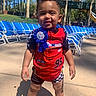 toddler, child, birthday_boy, red_outfit, racing_theme, blue_ribbon, poolside, lounge_chairs, water_slide, outdoor, sunny, smiling, happy, summer, footwear, shorts, standing, playground, trees, recreation