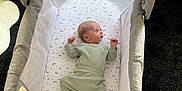 Arlo is registered to the contest to win money with this photo: baby, bassinet, blanket, carpet, clothing, cup, face, furniture, green_onesie, head, infant, mattress, person, portrait, sock, soft_toy, stars, moon, indoor, baby_sleeping