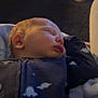 Arlo is registered to the contest to win money with this photo: baby, sleeping, infant, onesie, dinosaur_print, blanket, cozy, face, peaceful, child, indoor, soft_light, closeup, head, skin, cute, newborn, person, calm, resting