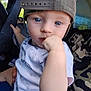 child, toddler, blue_eyes, cap, backwards_cap, white_shirt, car_prints, hand, fist, vehicle_interior, seat, adult, camouflage, curious, close_up, person, portrait, indoor, holding, baby