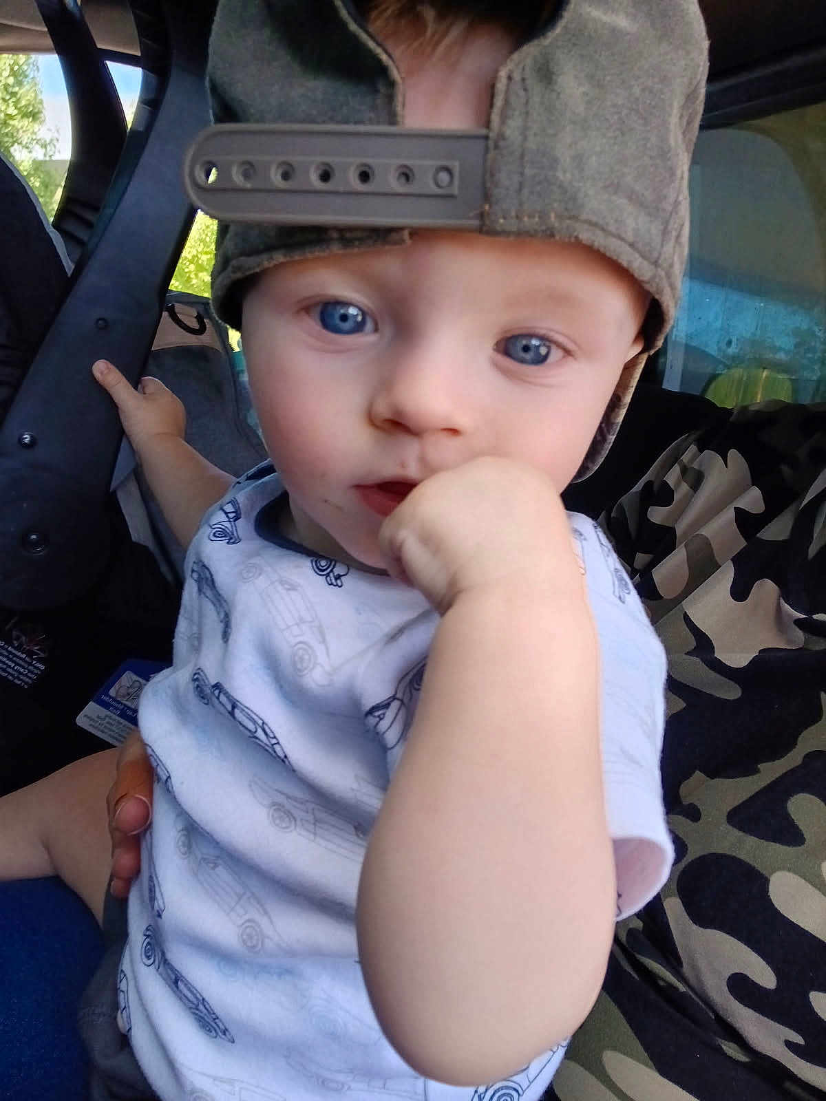 Hunter joined the competition — help win amazing prizes! child, toddler, blue_eyes, cap, backwards_cap, white_shirt, car_prints, hand, fist, vehicle_interior, seat, adult, camouflage, curious, close_up, person, portrait, indoor, holding, baby