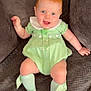baby, child, red_hair, blue_eyes, green_dress, socks, bow, smiling, tongue_out, sitting, couch, indoor, cute, happy, infant, person, apparel, fabric, plush, comfortable