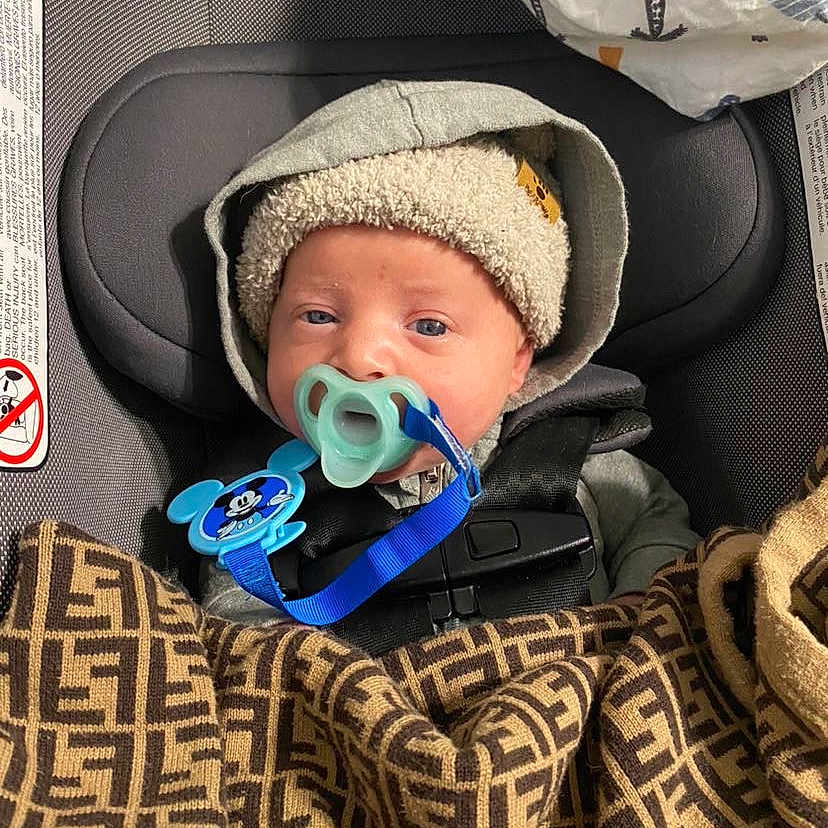 Elijah joined the competition — help win amazing prizes! baby, blanket, cap, car, clothing, coat, cushion, face, gun, hat, head, homedecor, jacket, person, photography, portrait, transportation, vehicle, weapon, yawning