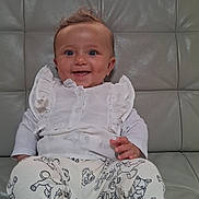 Shelby a rejoint le concours — aidez-le/la à gagner de superbes lots ! baby, child, smile, happy, cute, white_clothing, cat_pattern, pants, socks, couch, leather, indoor, portrait, sitting, young_child, frilly_top, person, face, hand, tooth