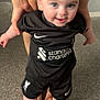 Matteo is registered to the contest to win money with this photo: baby, child, person, smiling, indoor, carpet, hands, black_clothing, socks, shorts, soccer_kit, nike_logo, standard_chartered_logo, liverpool_fc_logo, happy, cute, blue_eyes, short_hair, standing, supporting_hands