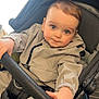 baby, child, stroller, seatbelt, hand, clothing, jacket, curly_hair, face, blue_eyes, portrait, infant, cute, indoors, person, grip, young_child, candid, expression, cozy