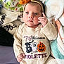 Violette is registered to the contest to win money with this photo: baby, infant, headband, orange_bow, onesie, halloween, ghost, pumpkin, spider_web, cute, portrait, indoors, blanket, soft, child, smiling, clothing, face, hands, lying_down