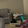 dog, small_dog, sweater, plastic_container, carpet, living_room, toy, baby_activity_table, plush_toy, purple_chew_toy, furniture, gray_chair, neutral_wall, floor_outlet, indoor, pet, cute, seated, looking_at_camera, cozy