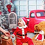 baby, child, santa_outfit, holiday, christmas, red_truck, wreath, gift_box, stuffed_toy, fur_bench, smiling, festive, indoor, decoration, hat, toy, hand, happy, seasonal, celebration