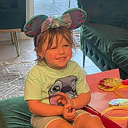 Thea joined the competition — help win amazing prizes! child, smile, mouse_ears, headband, tshirt, shorts, indoor, cushion, carpet, furniture, sofa, table, playful, happy, casual_clothing, home, person, cute, young, relaxed