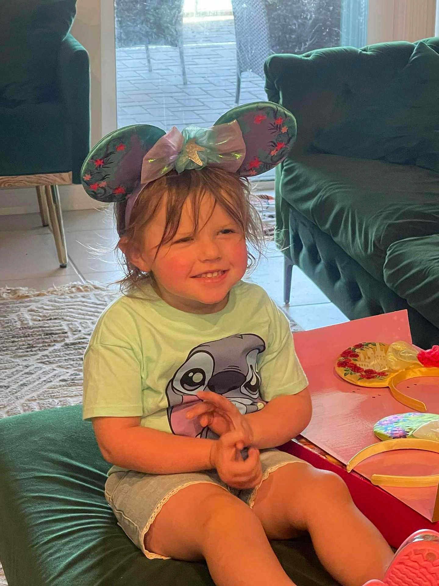 Thea joined the competition — help win amazing prizes! child, smile, mouse_ears, headband, tshirt, shorts, indoor, cushion, carpet, furniture, sofa, table, playful, happy, casual_clothing, home, person, cute, young, relaxed