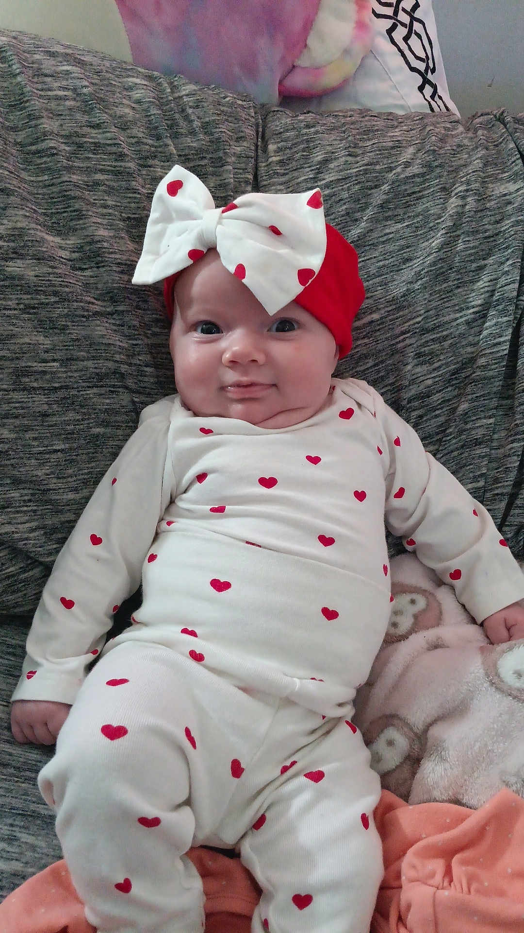 Neriah is registered to the contest to win money with this photo: baby, infant, heart_pattern, headband, bow, red, white, couch, blanket, cozy, smile, cute, clothing, sitting, indoors, child, face, expression, person, soft