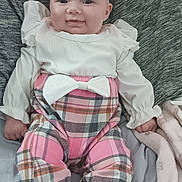Neriah is registered to the contest to win money with this photo: baby, child, smiling, headband, bow, plaid_pants, white_shirt, socks, blanket, soft_toy, couch, indoor, cute, portrait, infant, happy, sitting, cozy, clothing, person