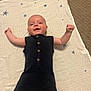 baby, infant, black_romper, blanket, stars, carpet, smiling, arms_up, lying_down, cute, child, indoor, young, happy, person, buttoned_clothing, head, face, skin, expression