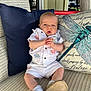 Grayson is registered to the contest to win money with this photo: baby, infant, child, white_outfit, shirt, shorts, socks, soft_shoes, pillow, dragonfly_pillow, navy_pillow, chair, patterned_chair, indoors, natural_light, hands_clasped, blue_eyes, cute, seated, portrait