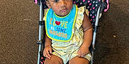 Maliya is registered to the contest to win money with this photo: baby, bib, braided_hair, carpet, child, clothing, curious, cute, expression, footwear, indoor, infant, person, polka_dot, portrait, sandals, sitting, stroller, toddler, young_child