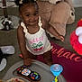 Maliya joined the competition — help win amazing prizes! baby, blanket, carpet, child, clothing, cute, floor, fun, hair_bows, home, indoor, person, playtime, remote_control, smiling, stuffed_animal, teddy_bear, toddler, toy, walker