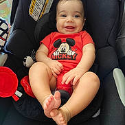 Samuel is registered to the contest to win money with this photo: baby, car_seat, mickey_mouse, red_clothing, smiling, child, infant, toy, black_fabric, seat_belt, cute, happy, feet, hands, indoor, person, portrait, baby_toys, child_seat, infant_clothing
