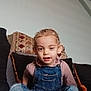 casual_clothing, child, comfortable, couch, cozy, curly_hair, cushions, denim_overalls, face, furniture, home, indoor, person, pink_shirt, portrait, relaxed, sitting, smiling, toddler, young_child
