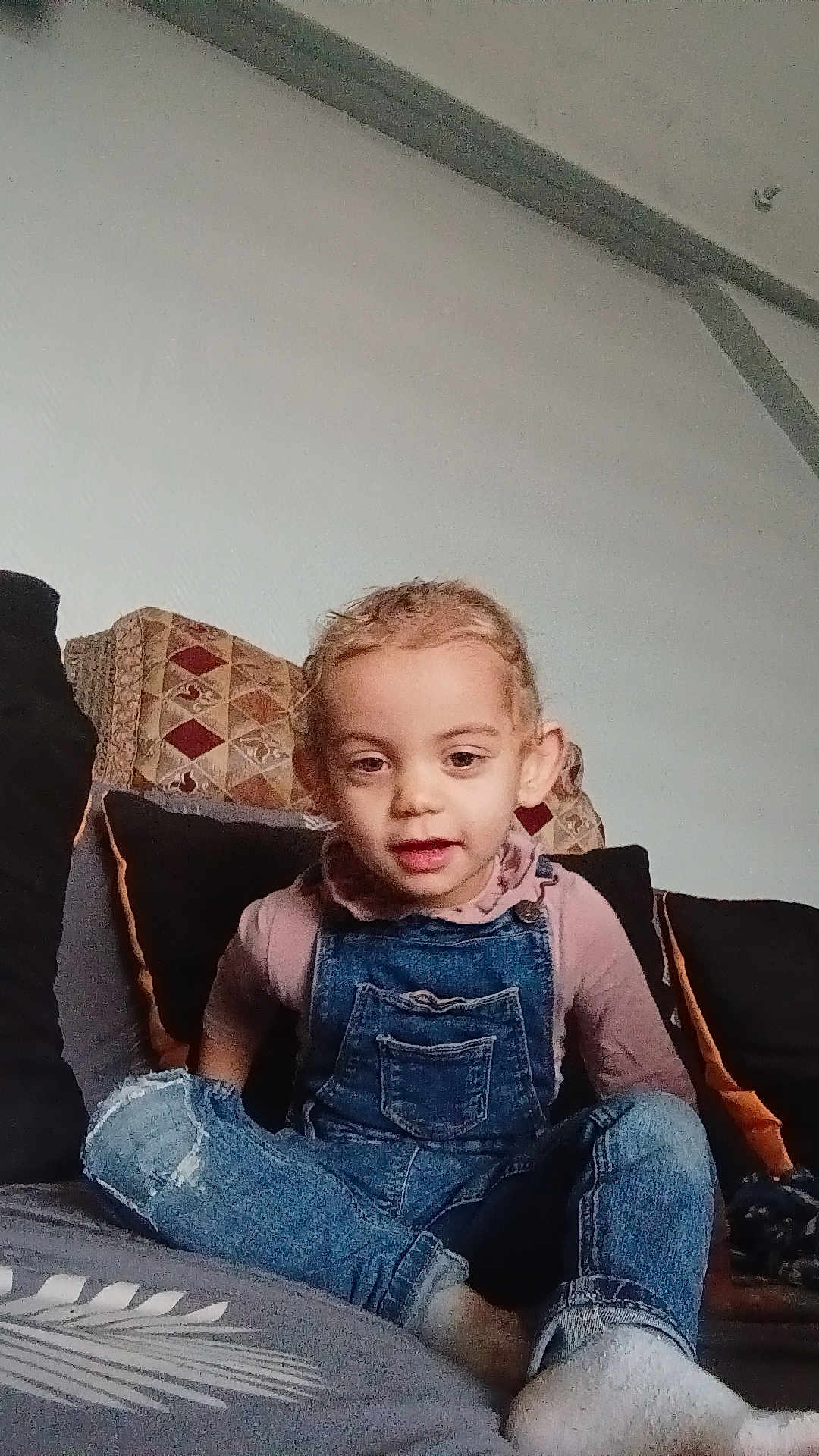 Ines participe au concours pour gagner de l'argent avec cette photo : toddler, child, denim_overalls, pink_shirt, couch, cushions, indoor, curly_hair, sitting, person, face, young_child, casual_clothing, home, relaxed, portrait, smiling, comfortable, furniture, cozy
