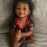 Josiah joined the competition — help win amazing prizes! toddler, child, smiling, curly_hair, sitting, clapping, black_clothing, red_trim, couch, gray_couch, indoors, happy, young_child, portrait, person, skin, face, eyes, hands, legs