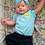 baby, blue_bow, blue_shirt, child, clothing, cute, fabric, floral_blanket, happy, headband, ice_cream_graphic, indoors, infant, lying_down, pattern, person, portrait, smiling_sun, soft_lighting, stretching_arm
