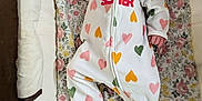 Line is registered to the contest to win money with this photo: baby, infant, pink_bow, onesie, hearts, floral_pattern, cushion, lying_down, face, hand, footed_pajamas, text, sleepwear, child, cute, indoor, portrait, soft_toys, newborn, headband