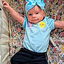 arms_outstretched, baby, blue_bow, child, cozy, cute, face, floral_blanket, happy, headband, ice_cream_print, indoors, infant, light_blue_shirt, lying_down, pants, portrait, smiling, soft_lighting, young_child