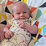 baby, infant, smile, onesie, patterned_clothing, geometric_pattern, cushion, colorful, indoor, child, face, hand, skin, cute, resting, portrait, person, plush, comfort, young