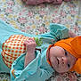 baby, infant, headband, orange_bow, turquoise_outfit, pumpkin_patch, hand, face, lying_down, bedspread, floral_pattern, cute, portrait, newborn, soft_light, clothing, person, indoors, smiling, child