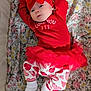 baby, infant, red_clothing, headband, bow, floral_blanket, pattern, lying_down, cute, toddler, white_socks, heart_pattern, tutu_skirt, child, portrait, indoors, soft_lighting, resting, young_child, cozy